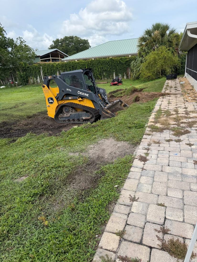 Skid steer cutting the pool pad into a back yard lawn next to a paved walkway