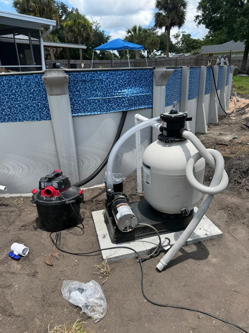Pump and sand filter set on level pads beside a partly assembled above-ground pool wall